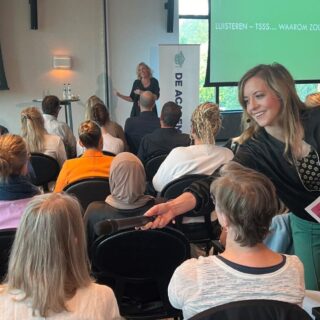 vrouw met microfoon in hand in een zaal vol mensen