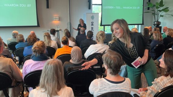 vrouw met microfoon in hand in een zaal vol mensen